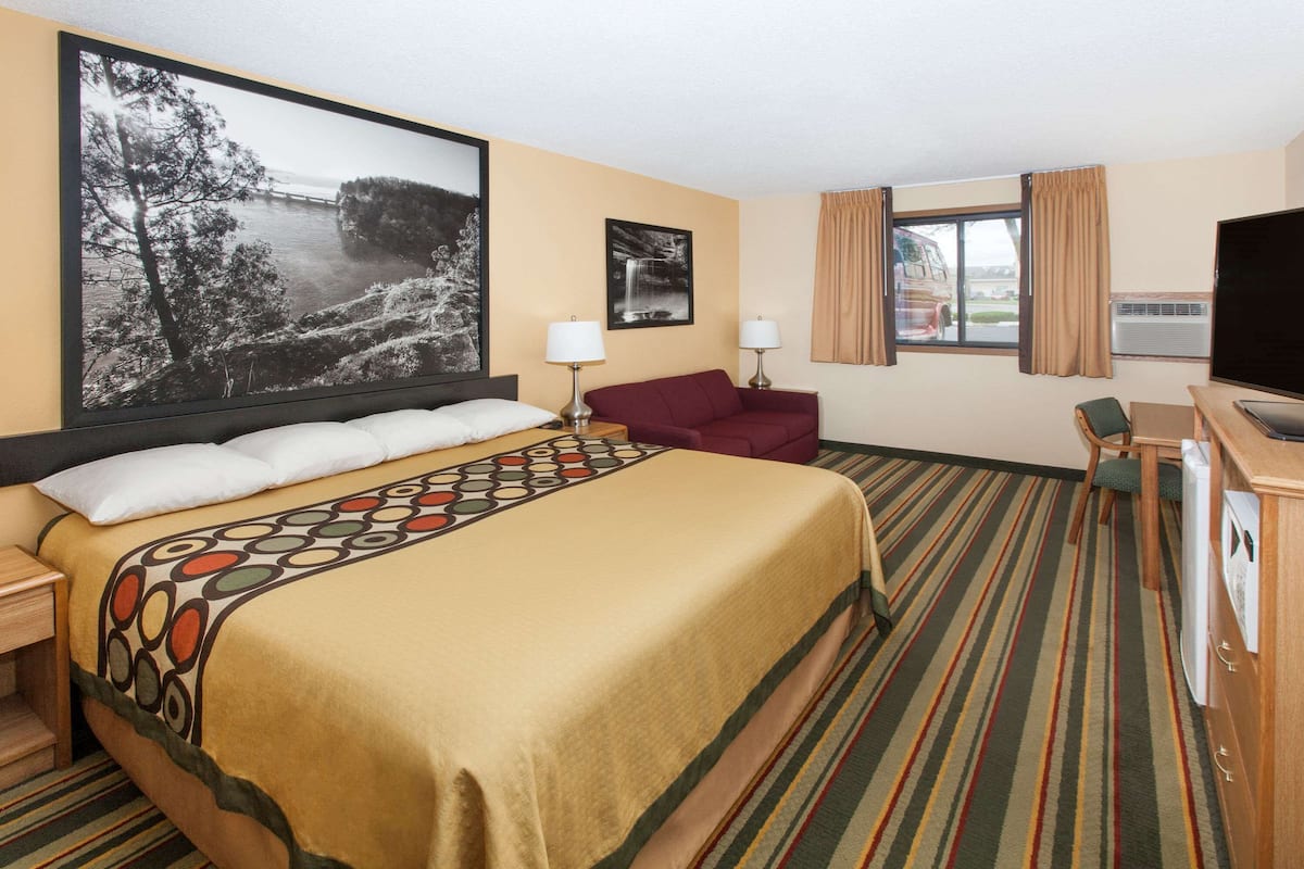 A hotel room with a large bed, a desk with a chair, a TV, and a window with curtains.