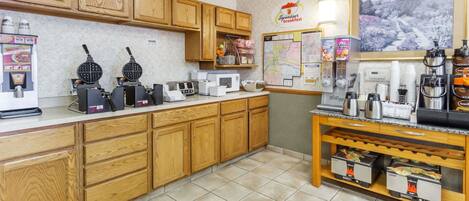 A kitchen with wooden cabinets, waffle makers, a coffee station, and a map on the wall.