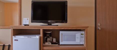 A kitchenette with a refrigerator, microwave, and a television on a wooden cabinet.
