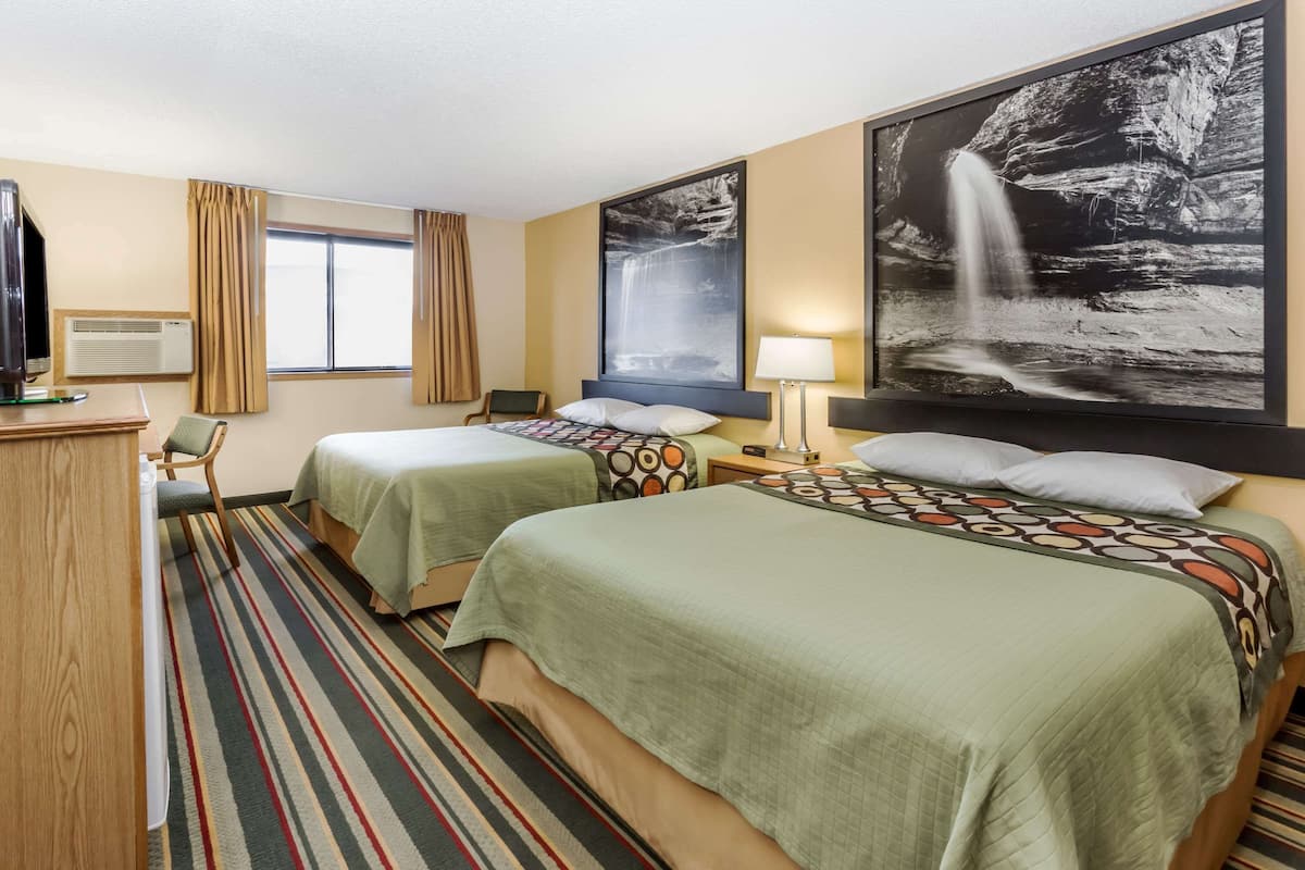 A hotel room with two beds, a desk, a chair, a TV, and a large waterfall painting on the wall.