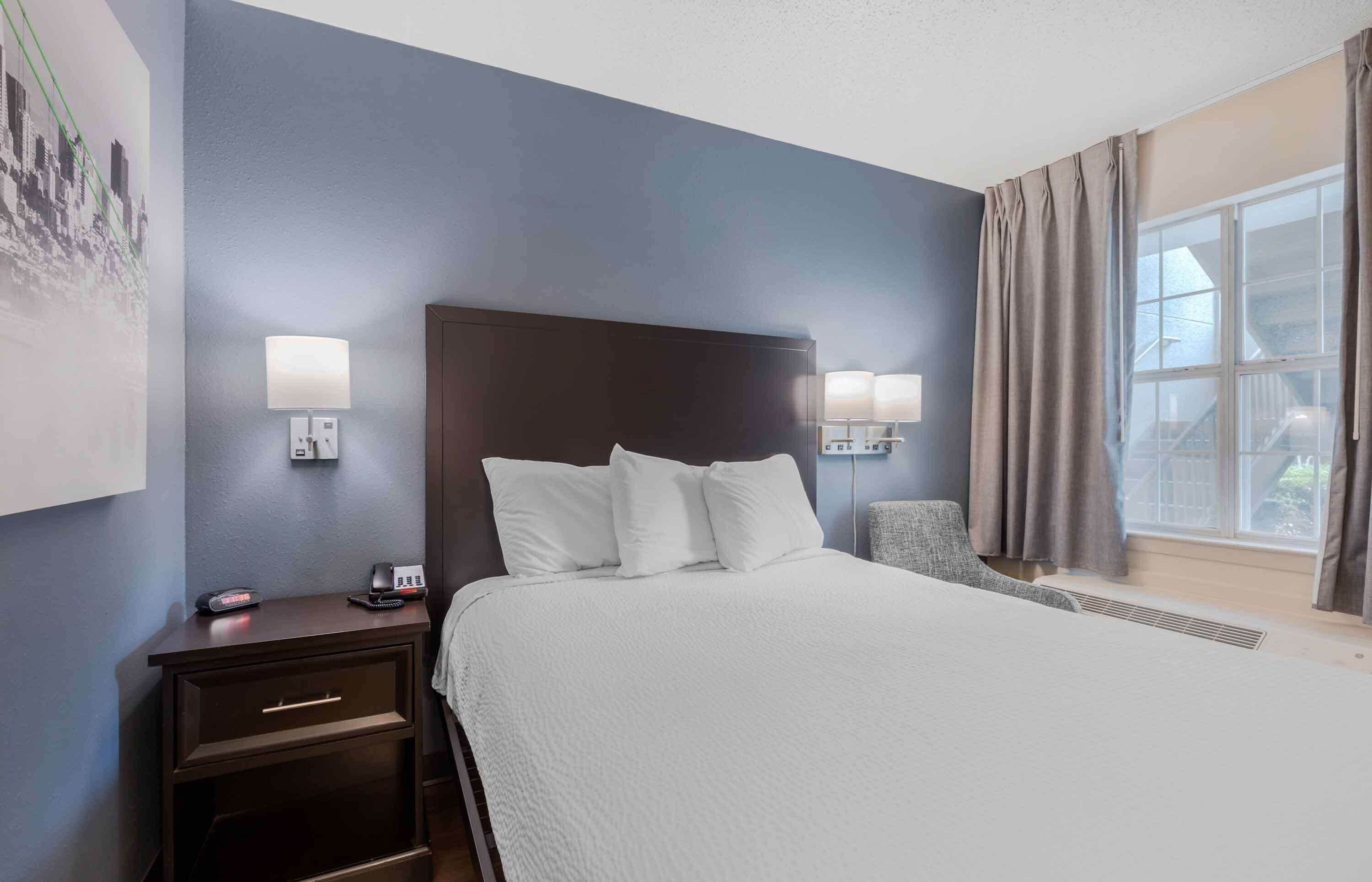 A hotel room with a large bed, two bedside tables with lamps, a chair, and a window with curtains.
