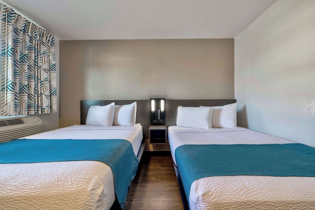 A hotel room with two beds, a wall-mounted TV, and a patterned curtain.