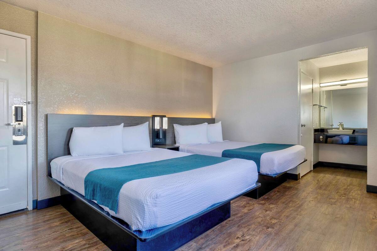 A hotel room with two beds, a bathroom with a mirror, and a wooden floor.