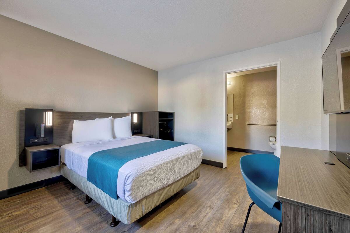 A hotel room with a bed, bedside tables, a desk, and a chair.