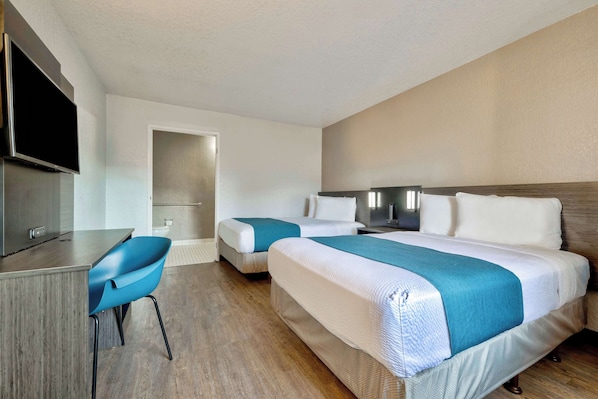 A hotel room with a desk, two beds, a TV, and a bathroom door.