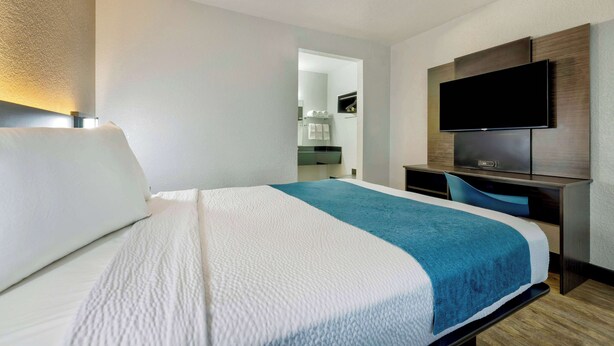 A hotel room with a bed, a desk, a flat-screen TV, and a mirror.