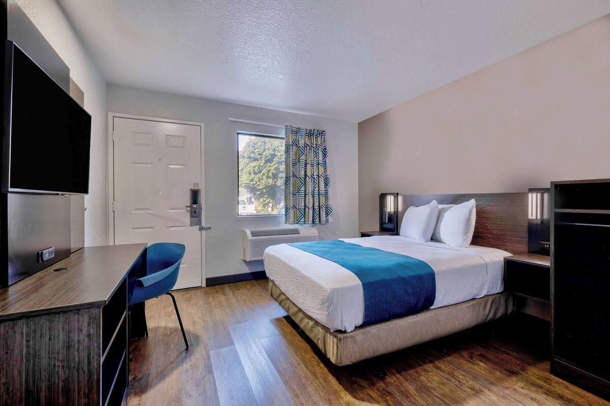 A hotel room with a bed, a desk, a chair, a TV, and a window with curtains.