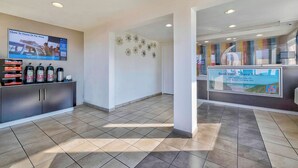 A hotel reception area with a digital screen displaying a travel advertisement, a coffee station, and a sign promoting a mobile app.