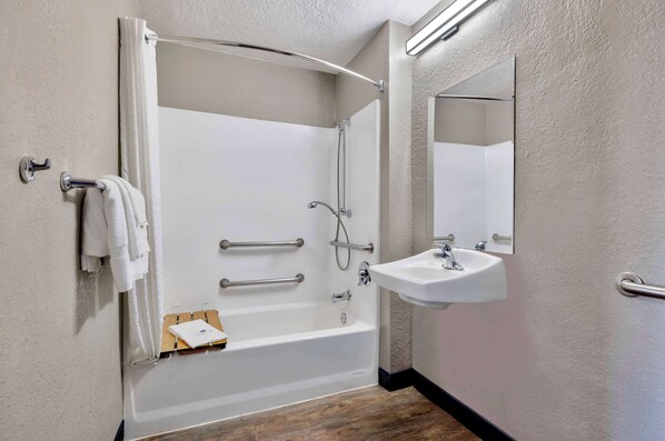 A modern bathroom with a bathtub, shower, and sink. There are grab bars, a towel rack, and a mirror.