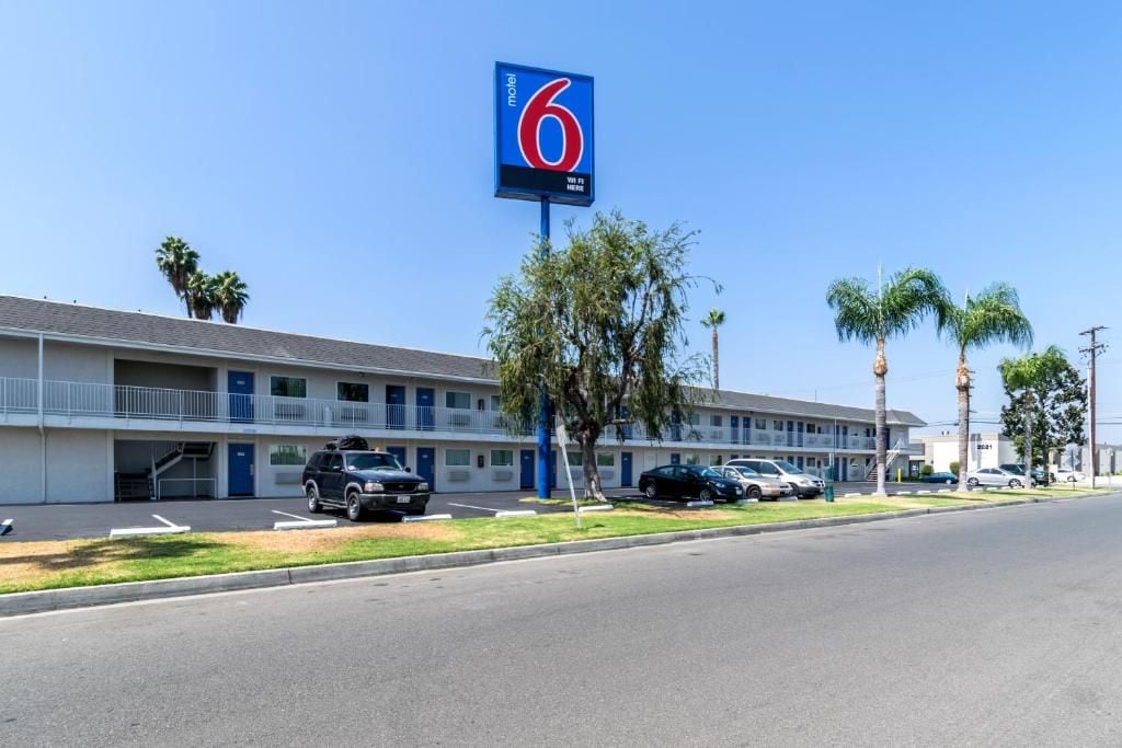 Un motel con un llamativo letrero con el número '6', un estacionamiento y un edificio con varias ventanas y balcones.