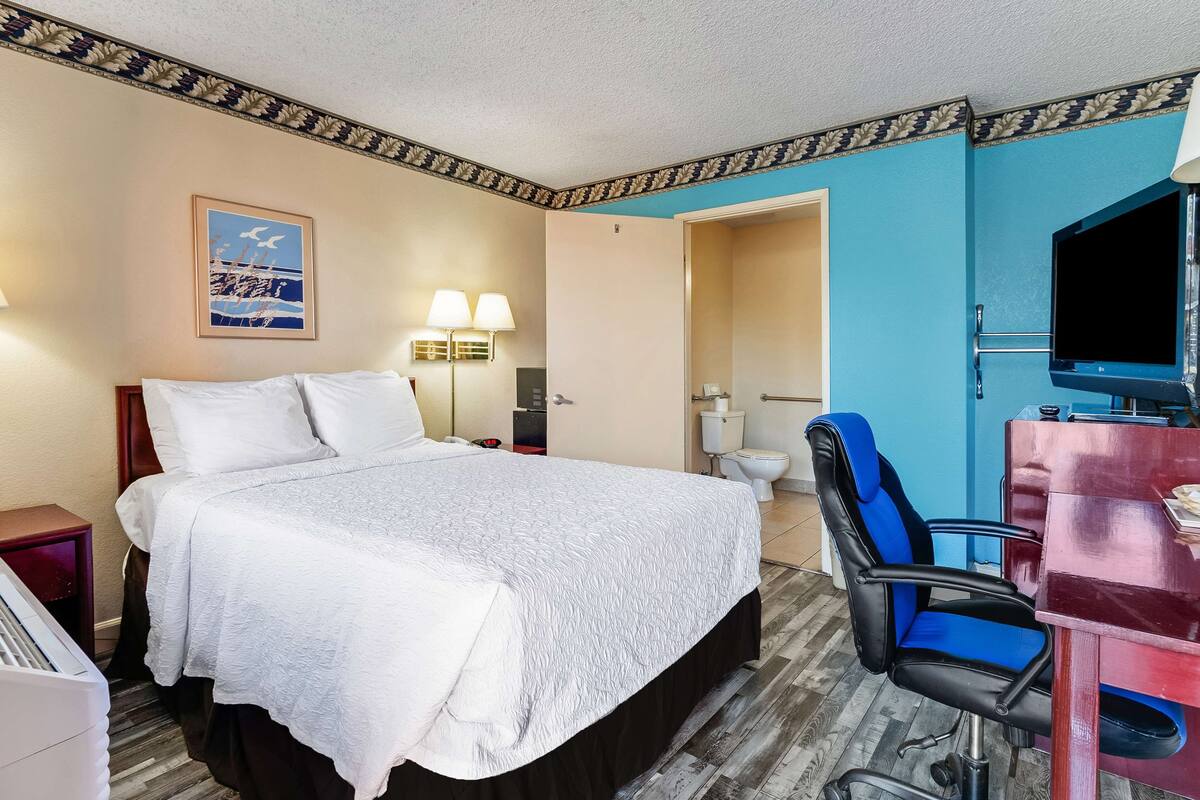 Habitación de hotel con una cama grande, un escritorio con silla, televisión y baño visible a través de una puerta abierta.