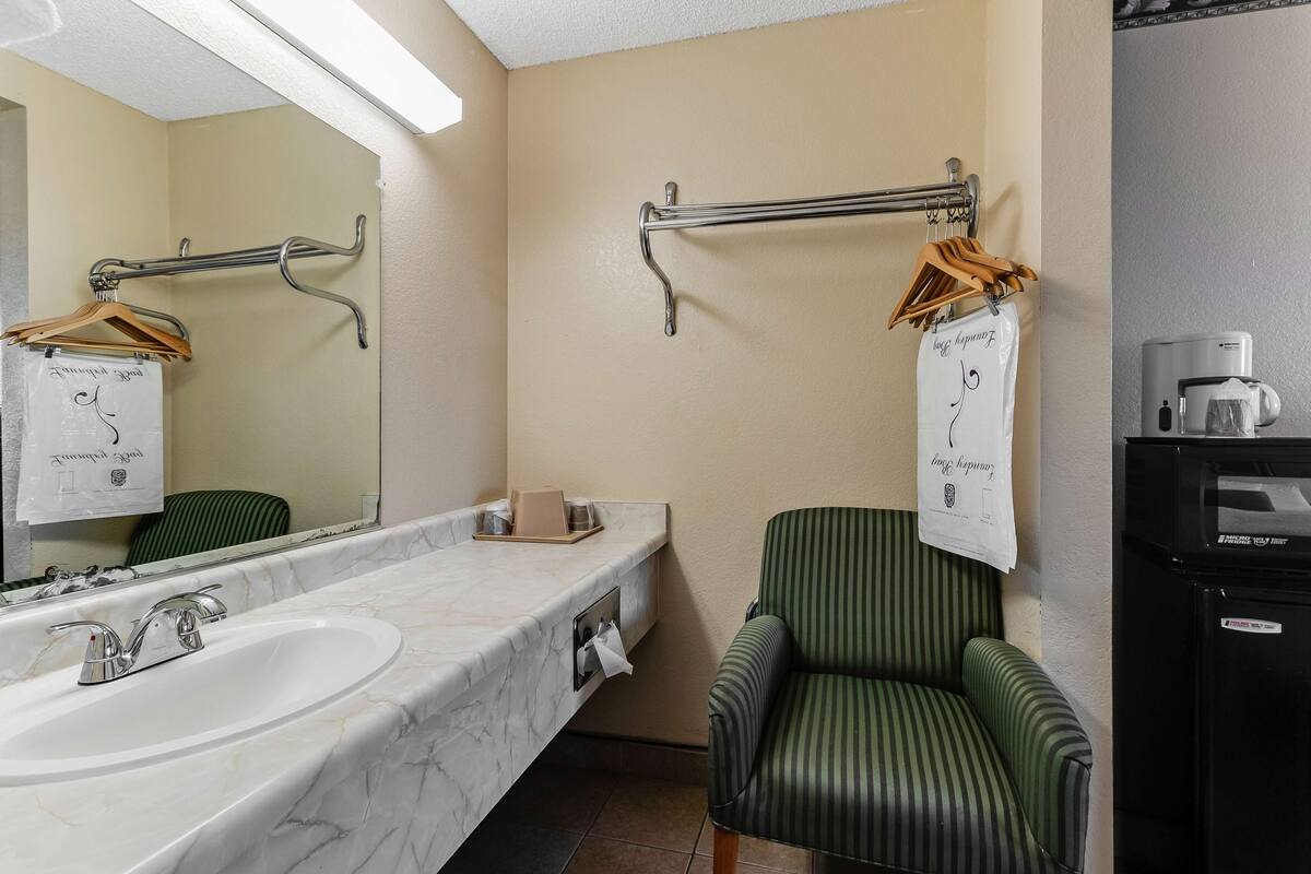 Un baño con lavamanos de mármol, una silla verde a rayas y un perchero con ganchos.