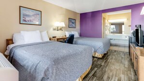 Habitación de hotel con dos camas, un escritorio con lámpara, televisión y baño visible a través de un arco.