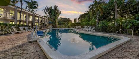 A swimming pool with lounge chairs, palm trees, and a building with balconies.