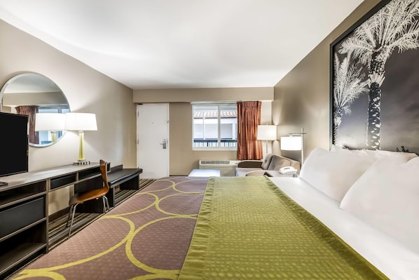 Habitación de hotel con cama, escritorio, silla, televisión y un ventanal con cortinas.