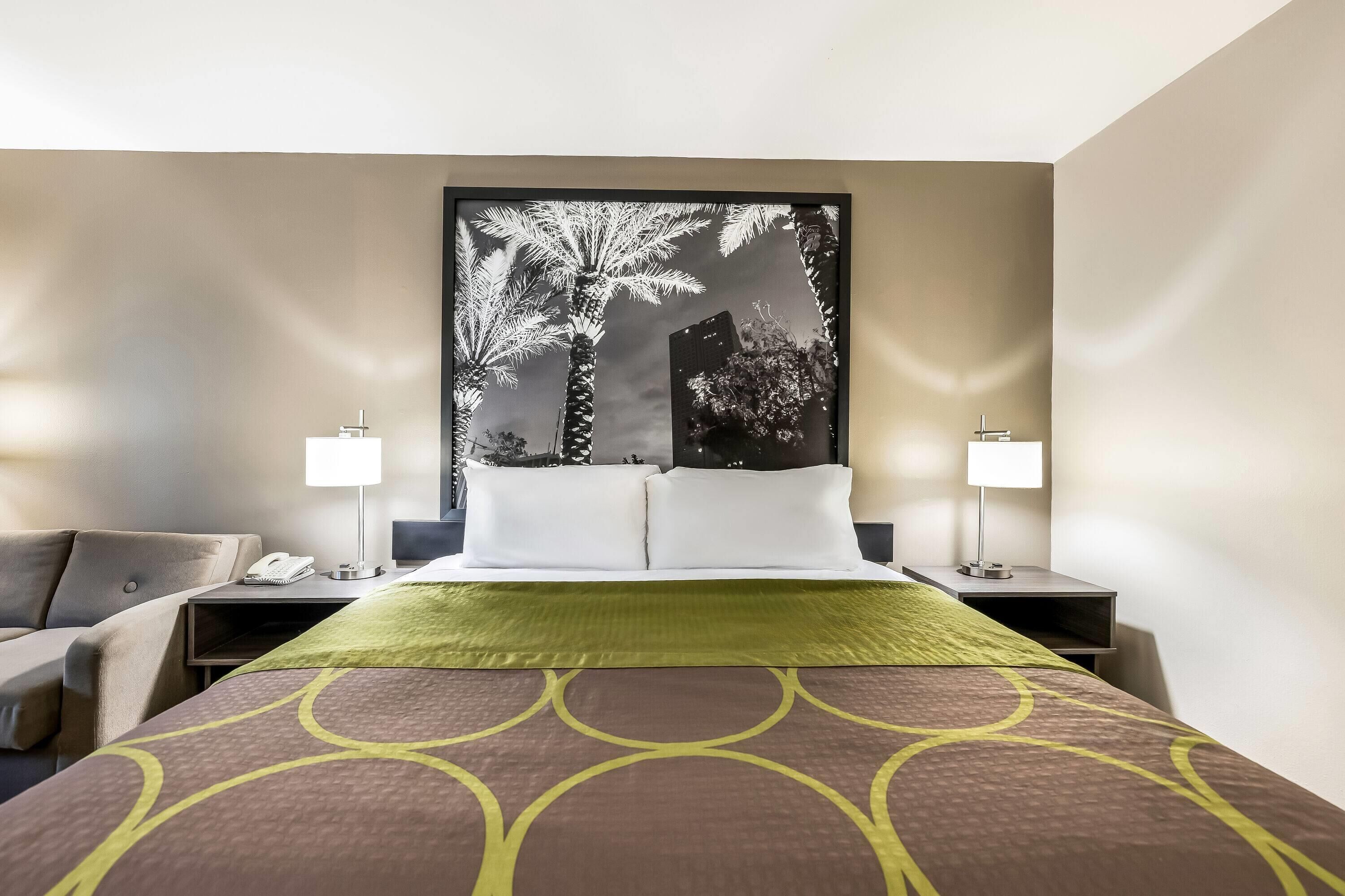 Una habitación de hotel con cama, dos mesitas de noche, una lámpara, una silla y una obra de arte grande en la pared.