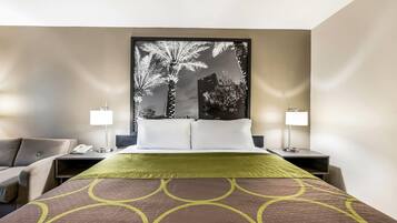 Una habitación de hotel con cama, dos mesitas de noche, una lámpara, una silla y una obra de arte grande en la pared.