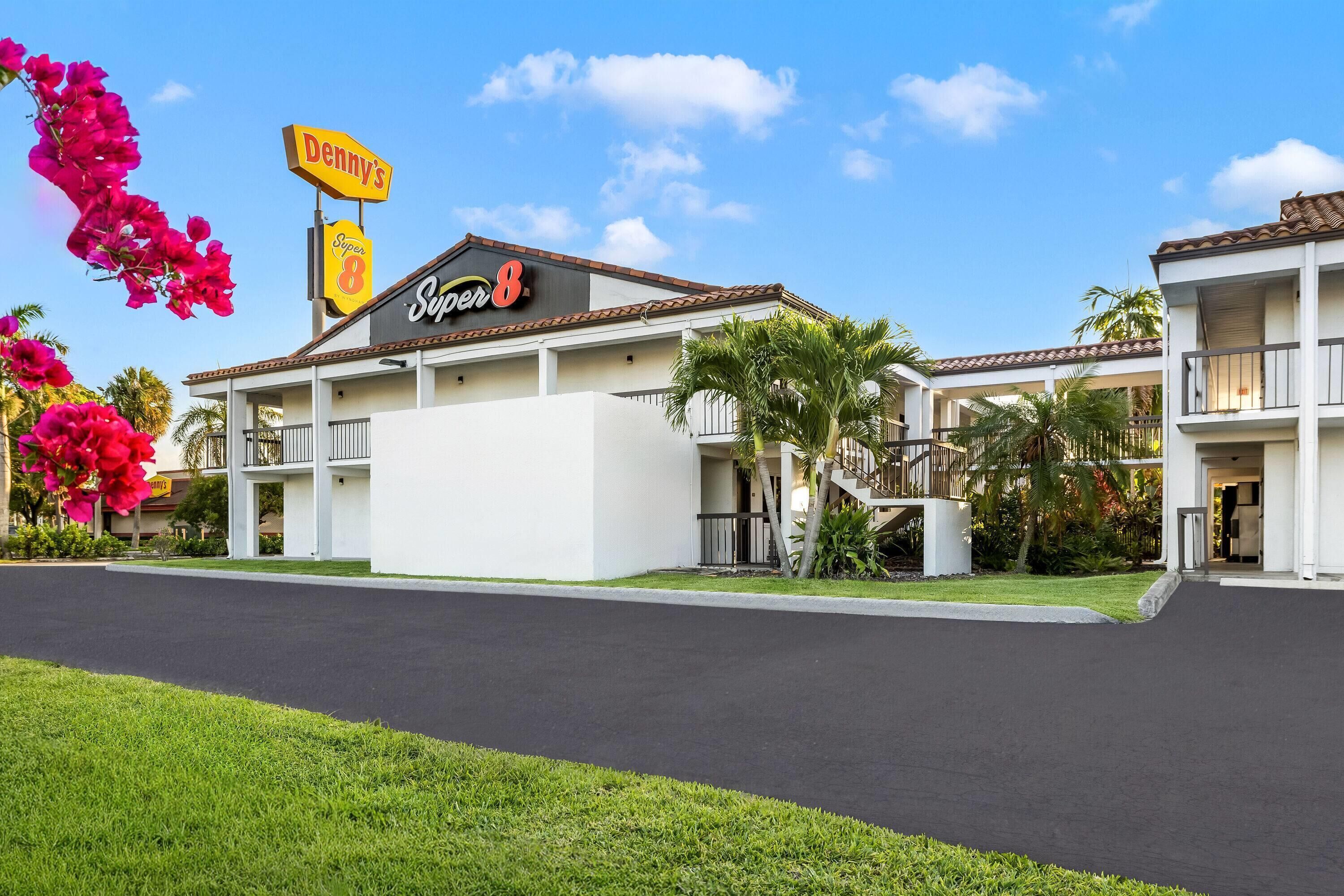 A hotel with a sign reading 'Denny's Super 8' and a covered outdoor area with palm trees.