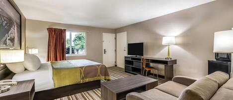 Quarto de hotel com cama, sofá, secretária e televisão, além de janela com cortinas.
