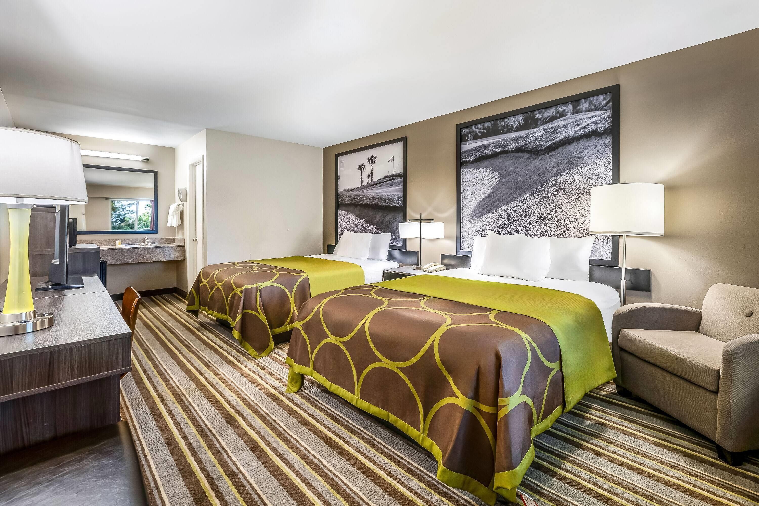 A hotel room with two beds, a desk, a chair, and a large window.