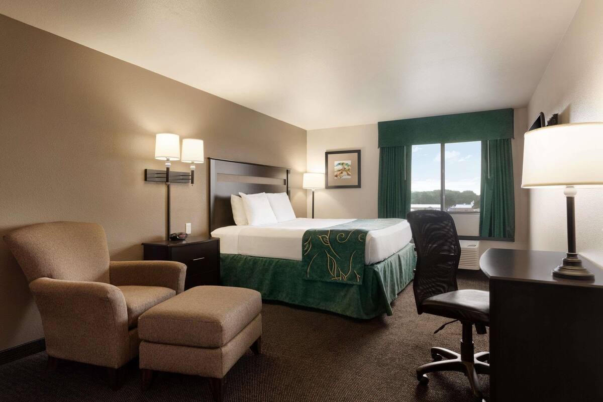 A hotel room with a bed, a chair, a desk, and a window with curtains.