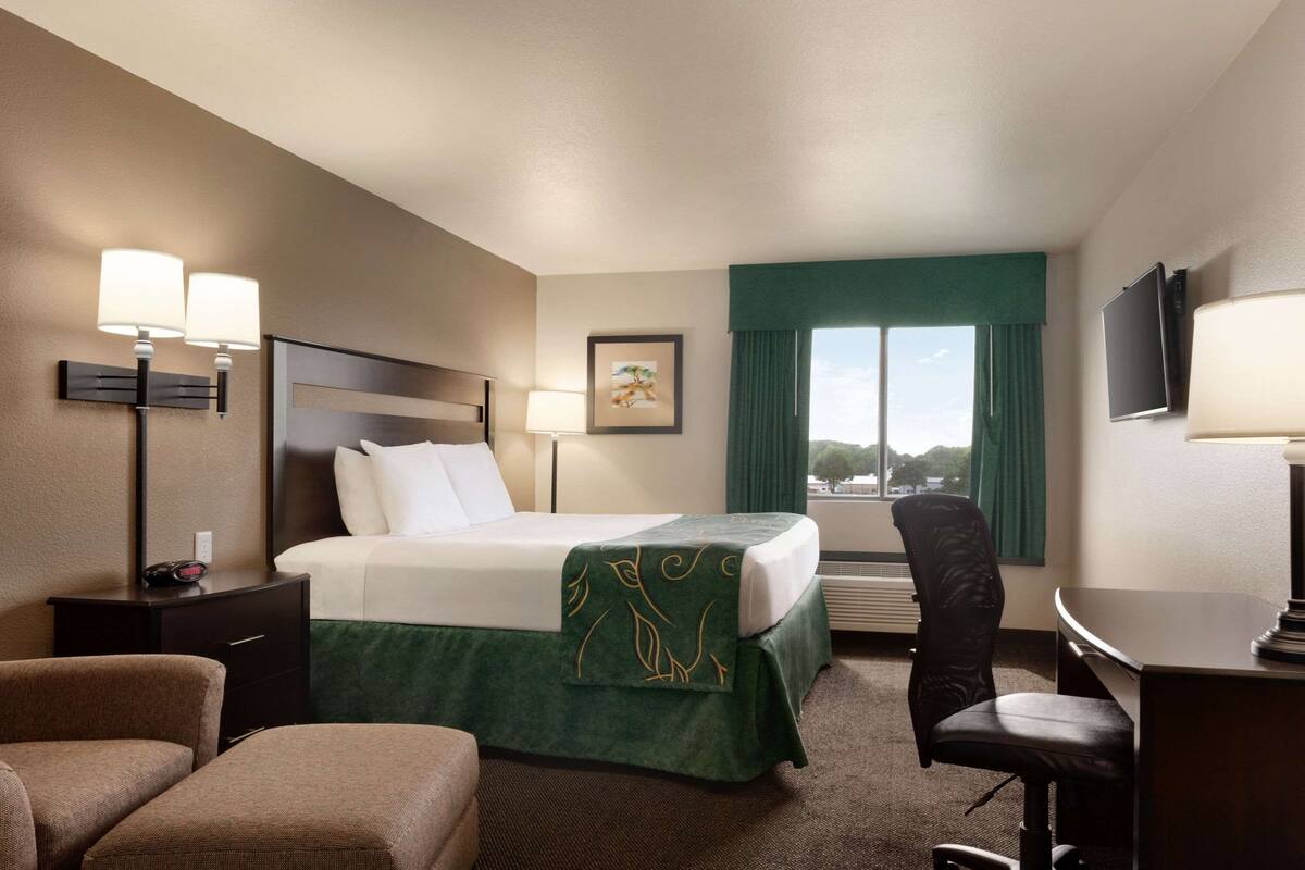 A hotel room with a bed, a desk, a chair, a TV, and a window with curtains.