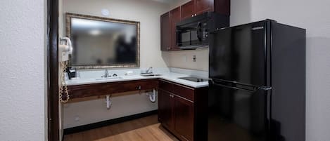 A compact kitchen with a black refrigerator, a microwave, and a double sink with a vanity mirror.