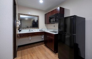 A compact kitchen with a black refrigerator, a microwave, and a double sink with a vanity mirror.