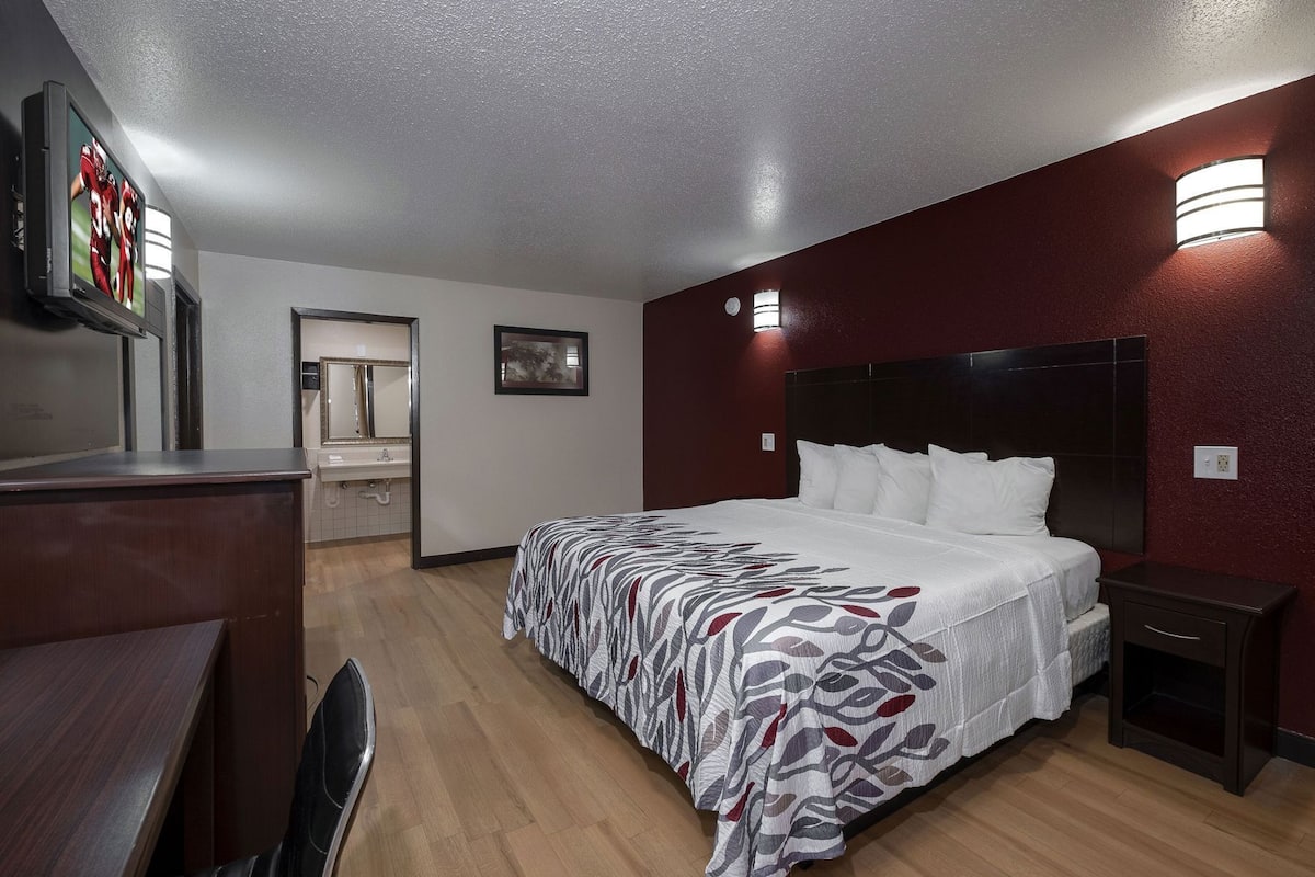 A hotel room with a bed, bedside tables, a desk, a mirror, and a TV.