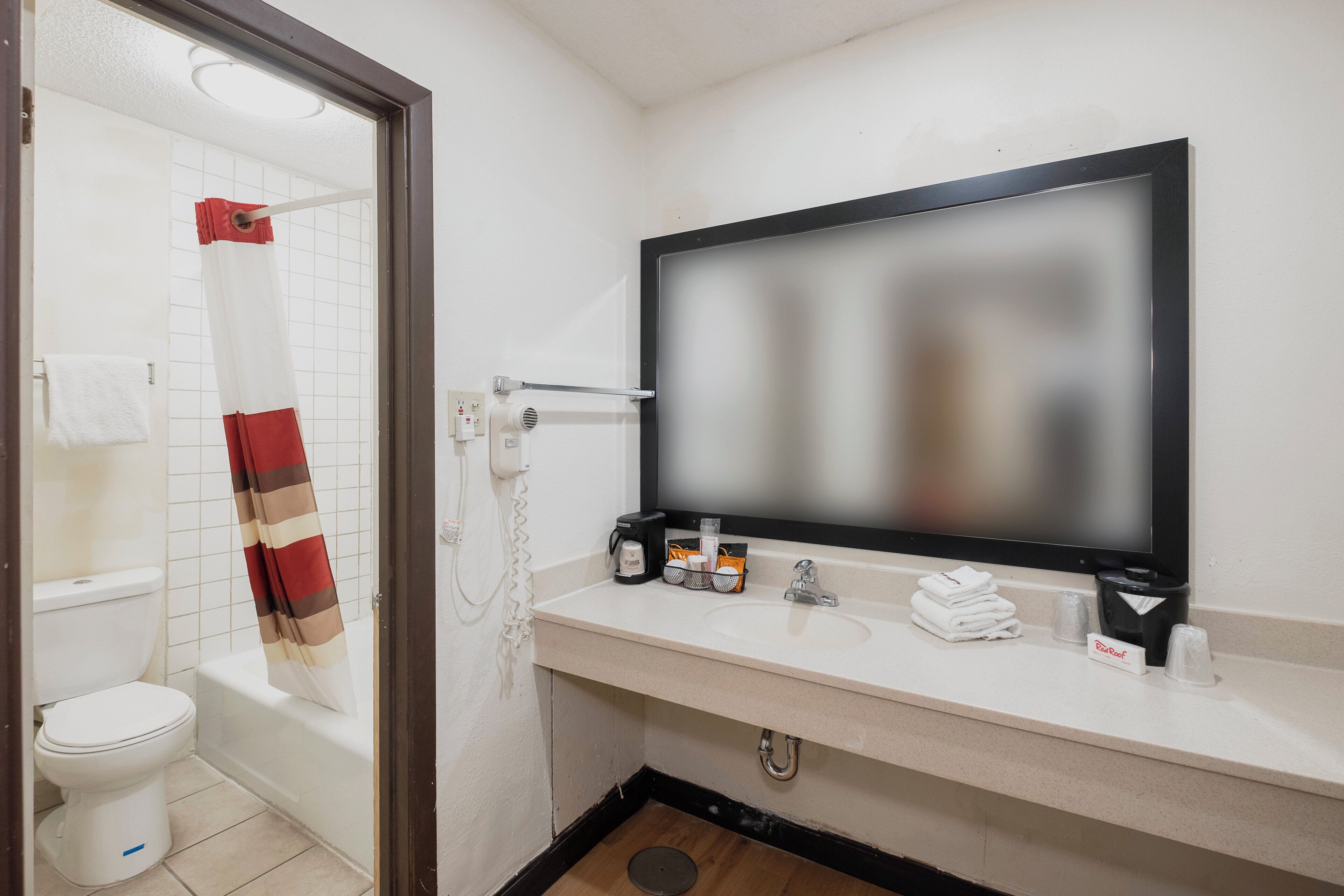 Un baño con inodoro, ducha, lavamanos con espejo y toallero.