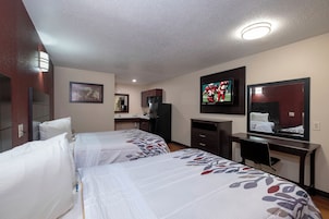 A hotel room with two beds, a desk, a television, and a bathroom.