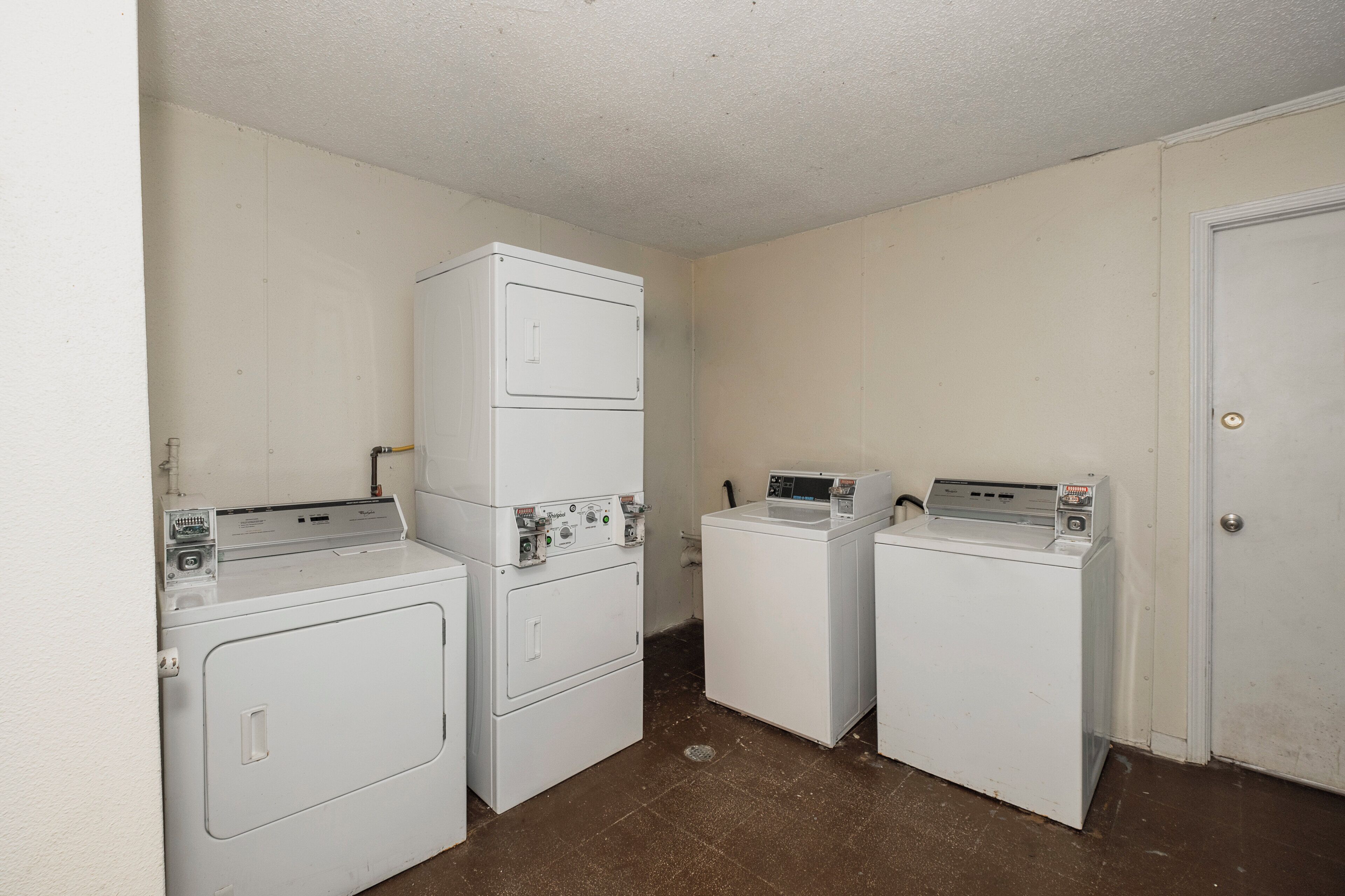 A laundry room with two stacked washers and dryers, a door, and a wall-mounted control panel.