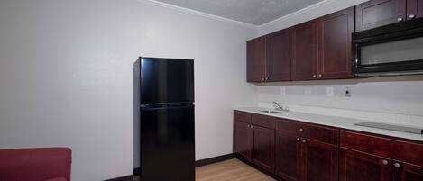 Una cocina compacta con un refrigerador negro, muebles de madera, una encimera blanca y una silla roja.