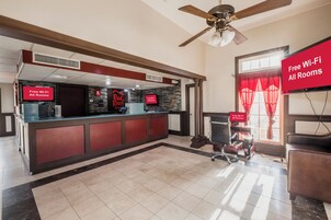 A hotel lobby with a reception desk, a ceiling fan, and a sign indicating free Wi-Fi in all rooms.