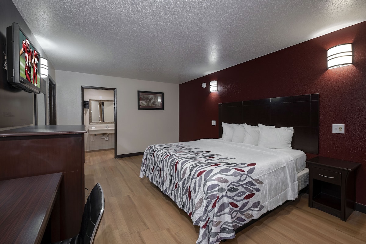 A hotel room with a large bed, a desk, a chair, a TV, and a bathroom visible through an open door.