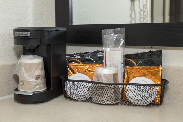 A coffee maker and a basket with items like a mug, a glass, and plastic bags on a countertop. - Red Roof Inn Morgan City (Morgan City)