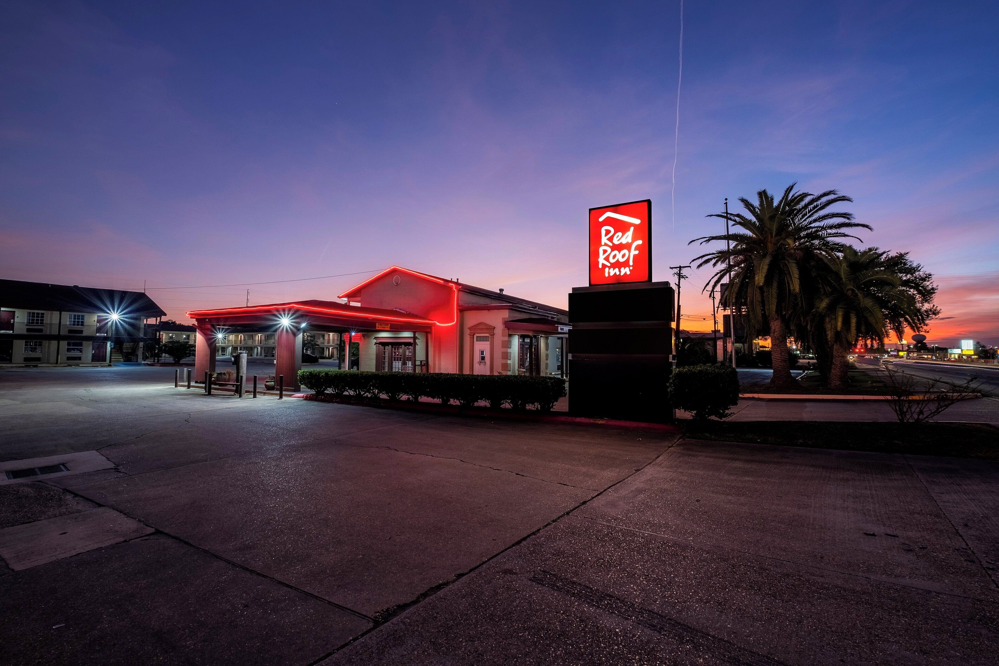 A Red Roof Inn with a prominent red neon sign, a covered parking area, and palm trees in the foreground.