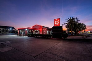 A Red Roof Inn with a prominent red neon sign, a covered parking area, and palm trees in the foreground. - Red Roof Inn Morgan City (Morgan City)