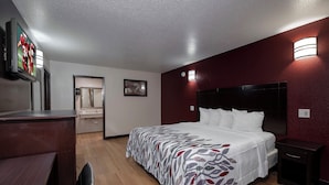 A hotel room with a bed, bedside tables, a desk, a mirror, and a television. - Red Roof Inn Morgan City (Morgan City)
