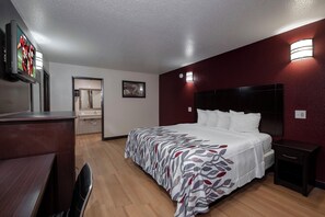 A hotel room with a bed, bedside tables, a desk, a mirror, and a television. - Red Roof Inn Morgan City (Morgan City)