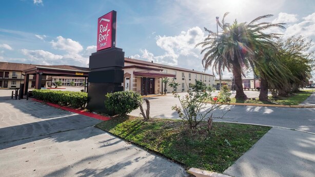 A hotel entrance with a prominent sign, a parking lot, and a palm tree. - Red Roof Inn Morgan City (Morgan City)