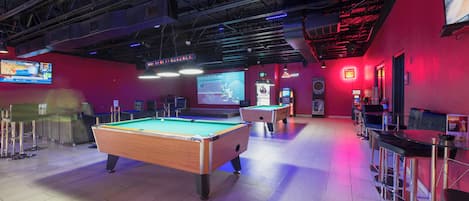 Ein Billardtisch mit Dartscheibe und Fernseher in einem Raum mit roten Wänden und hoher Decke.
