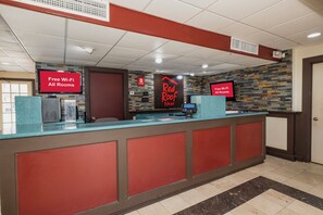 A hotel reception area with a modern design, featuring a reception desk, a digital screen displaying 'Free Wi-Fi All Rooms,' and a sign for 'Red Roof Inn.' - Red Roof Inn Morgan City (Morgan City)