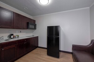 A kitchen with dark wooden cabinets, a black refrigerator, and a microwave.