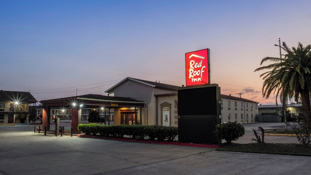 A Red Roof Inn with a prominent red neon sign, a parking lot, and a building with a flat roof and a small porch area. - Red Roof Inn Morgan City (Morgan City)
