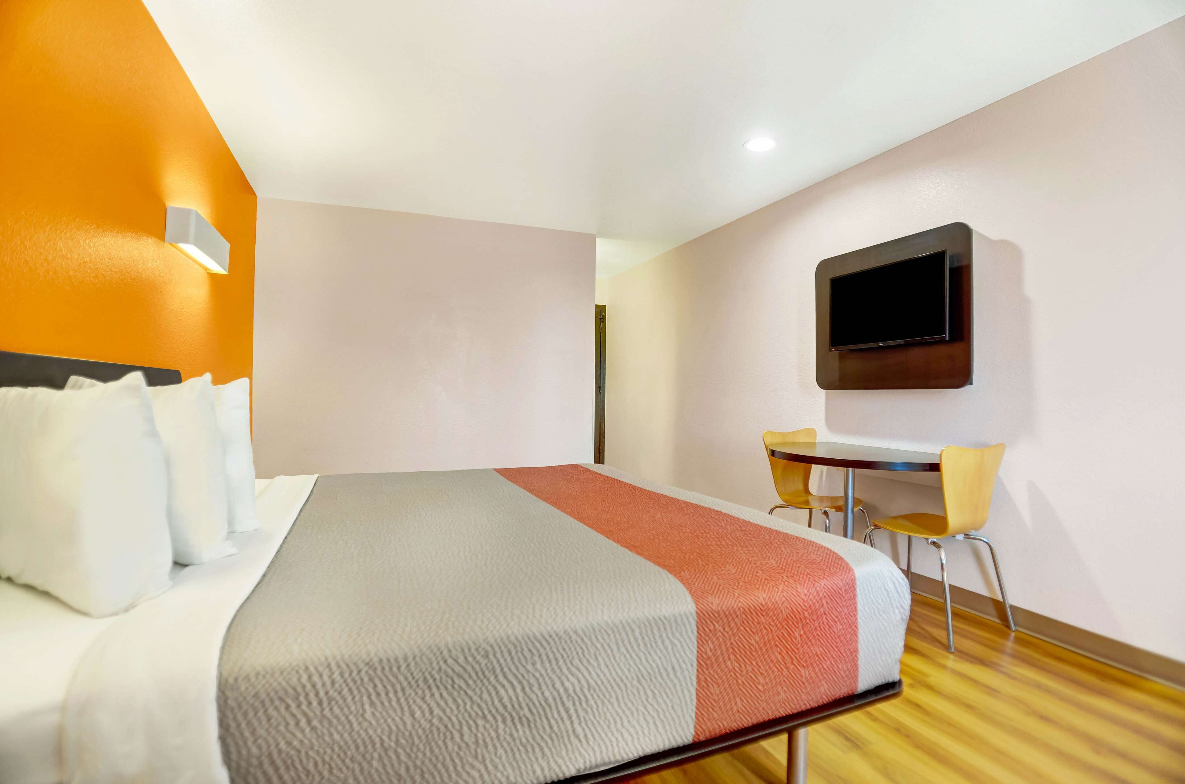 A hotel room with a bed, a desk, a chair, and a television mounted on the wall.