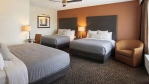 Una habitación de hotel con dos camas, una silla, un escritorio con lámpara y un ventilador de techo.