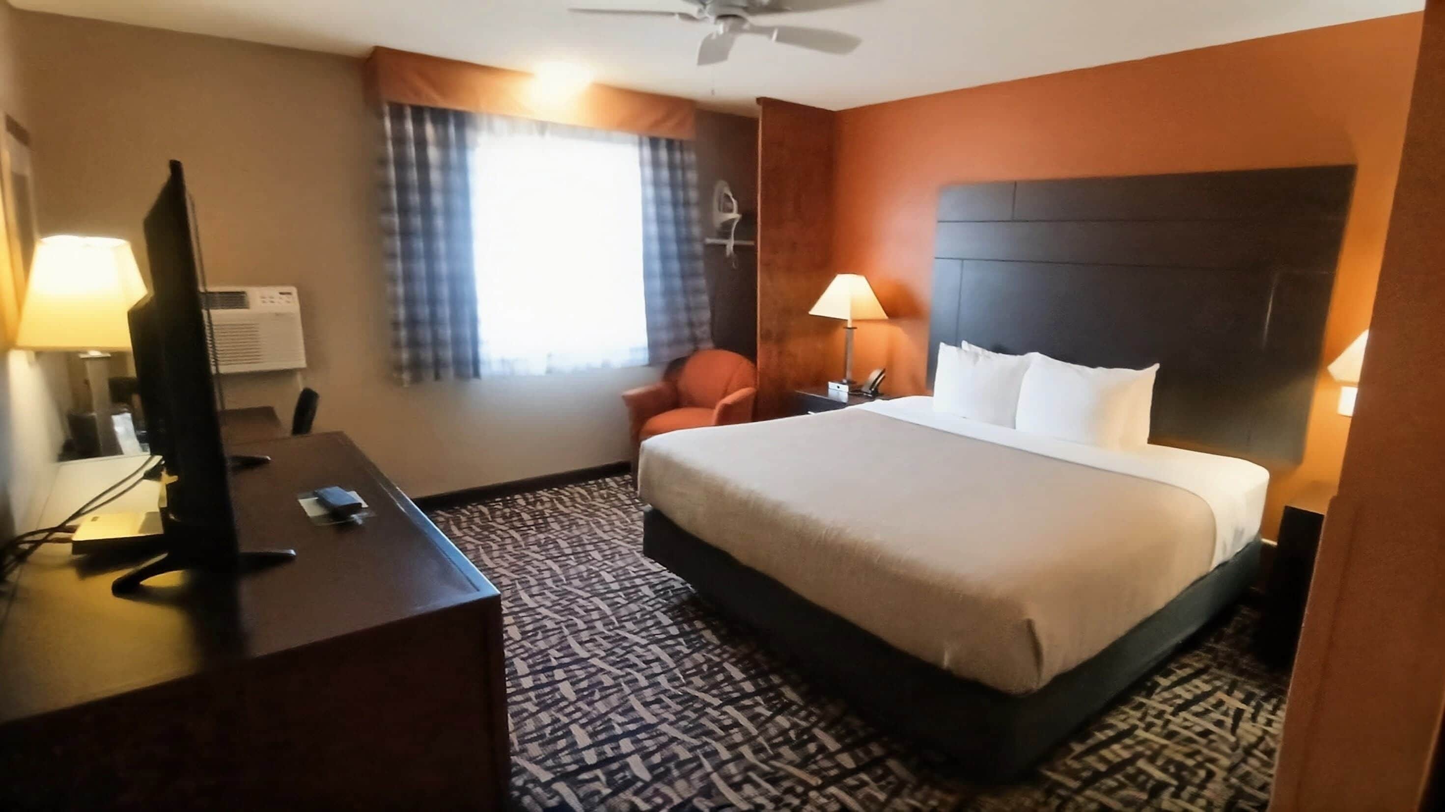 A hotel room with a bed, desk, chair, and a television.