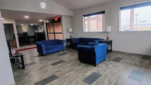 Un hall de hotel con mostrador de recepción, dos sofás azules, un ventanal con vistas y un atril para revistas.