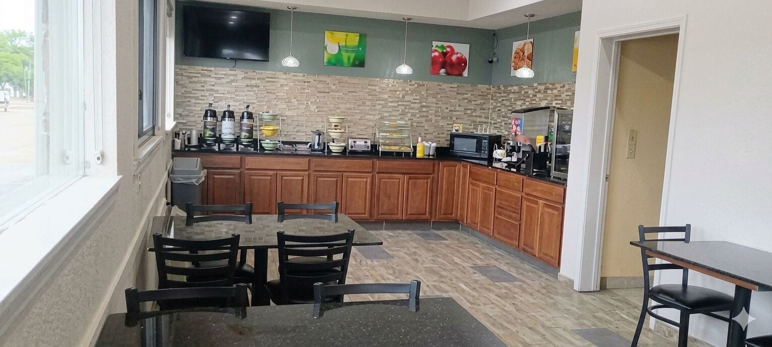 A kitchen with wooden cabinets, a tiled backsplash, and a dining area with tables and chairs.
